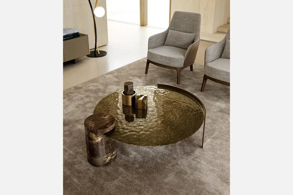 Stylish coffee table with a round, textured glass top and a decorative object on it, surrounded by two gray chairs.